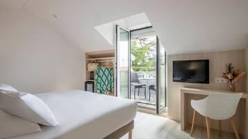 Un dormitorio moderno con cama, escritorio y televisor, y vista al exterior.