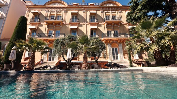 A hotel with a pool, palm trees, and outdoor seating. - Golden Tulip Cannes hotel de Paris (Cannes)