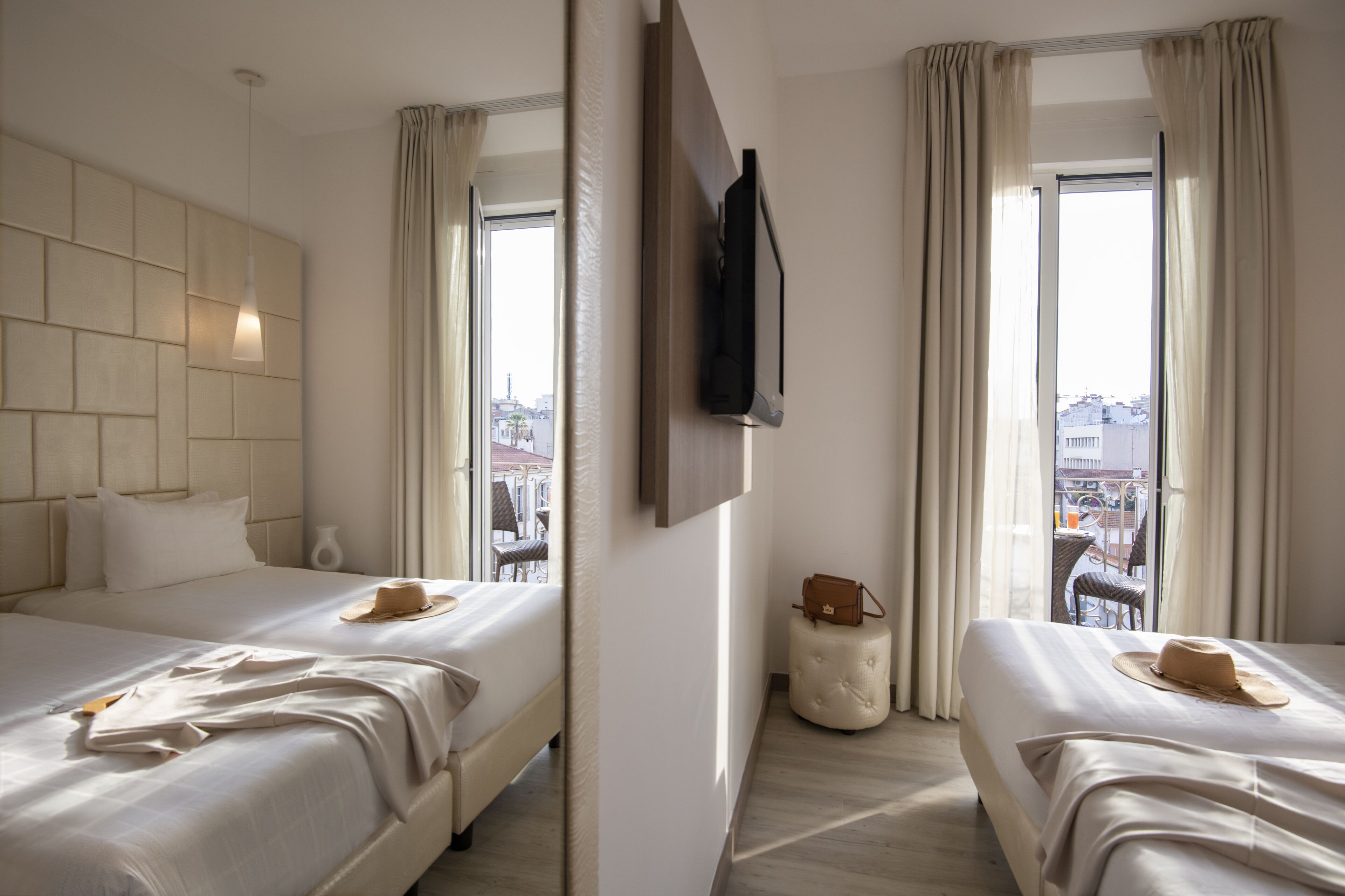 A hotel room with two beds, a TV mounted on the wall, and a view of the city through large windows.