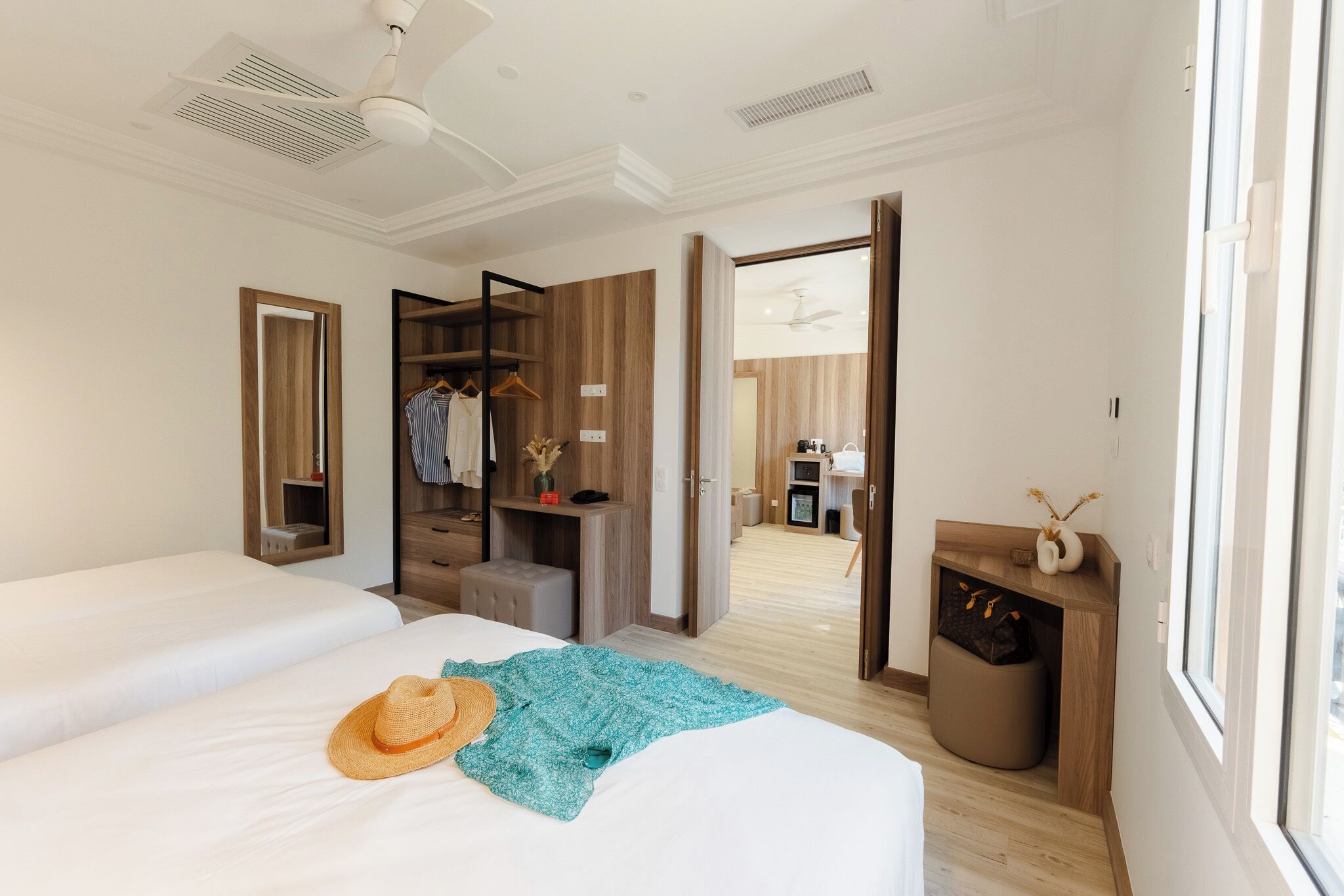 A hotel room with two beds, a wardrobe, a vanity, and a view of the hallway.