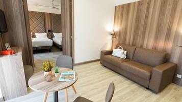 A hotel room with a bed, a sofa, a dining table with chairs, a small plant, and a magazine.