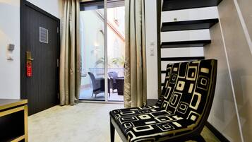 A modern room with a dark wooden door, a patterned armchair, a small table, and a view of an outdoor balcony.