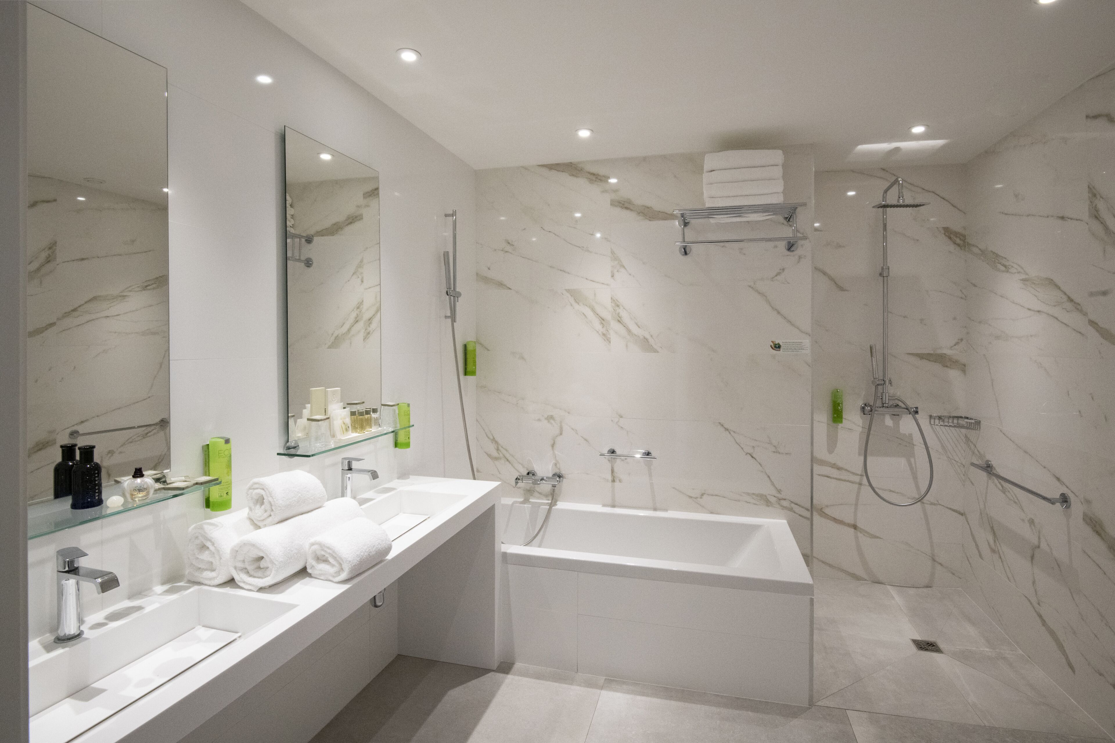 A modern bathroom with a large mirror, two sinks, a bathtub, and a shower.