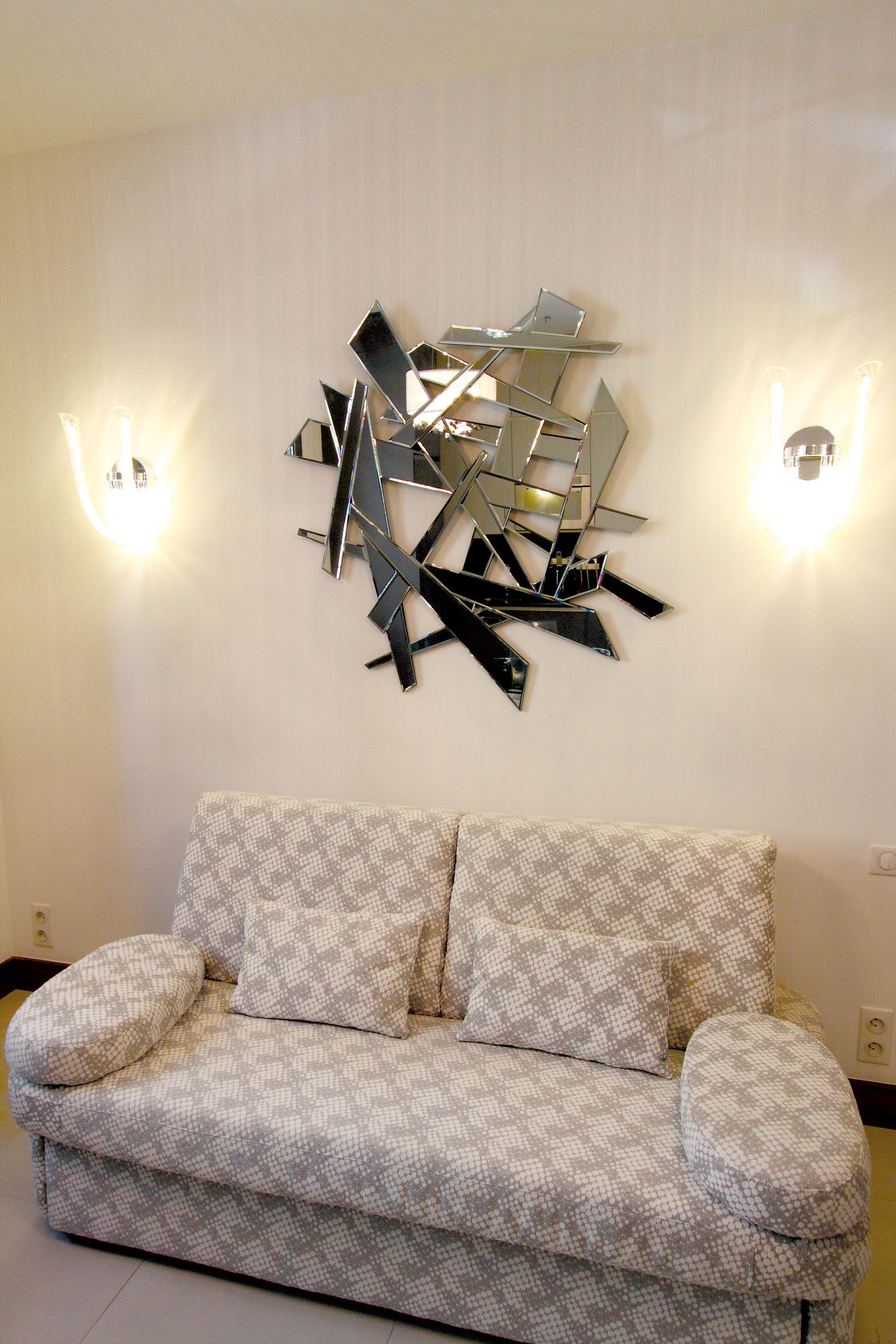 A modern living room with a patterned sofa, abstract wall art, and wall-mounted lighting.