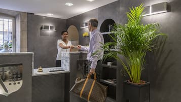 Una recepción con mostrador de mármol, una planta grande en maceta y una lámpara moderna fijada a la pared.