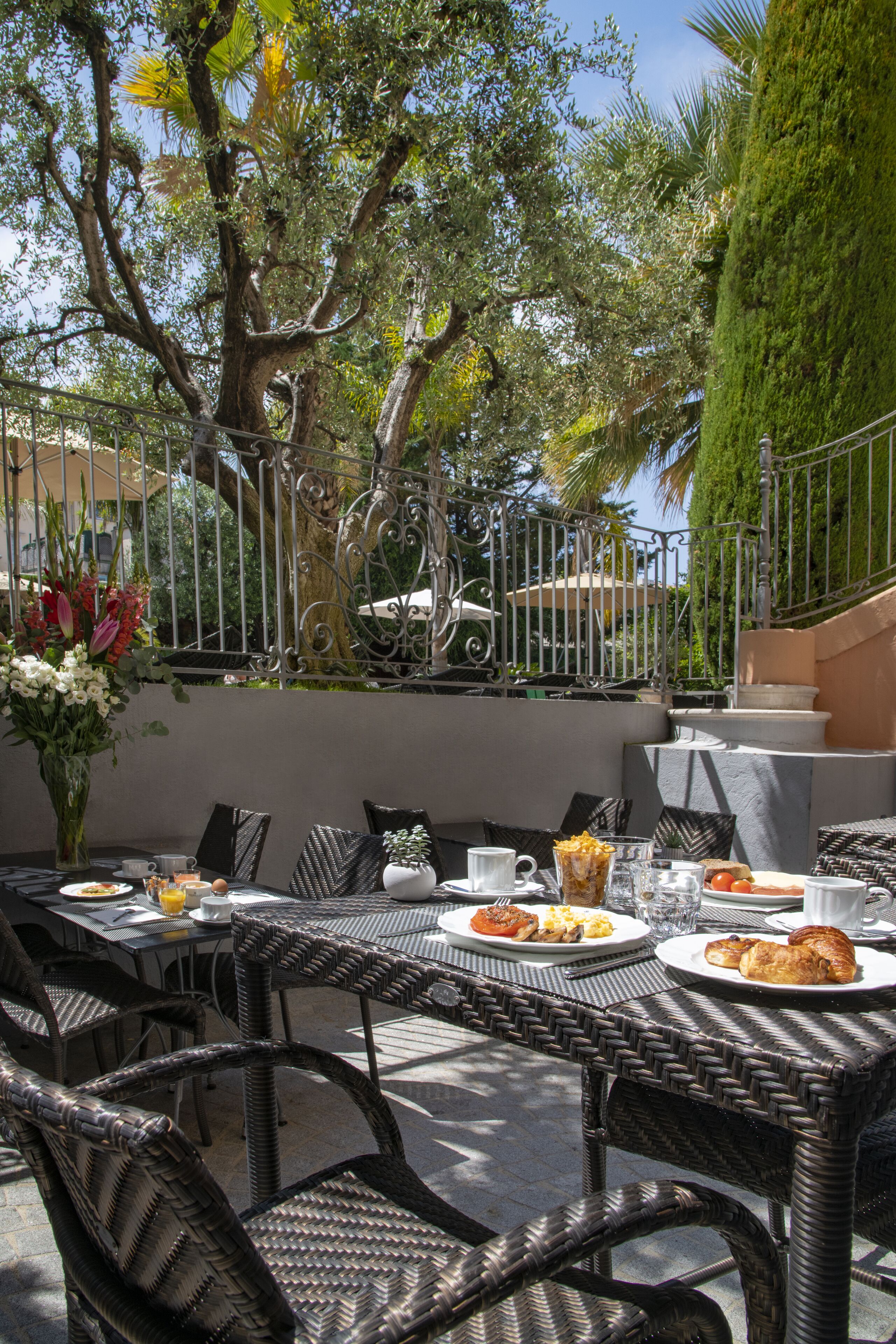 An outdoor dining area with wicker tables and chairs, a variety of dishes, and a decorative vase of flowers.