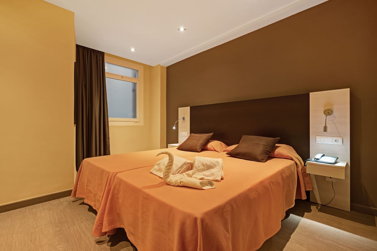 Una habitación de hotel con una cama grande, una mesita de noche con lámpara y una ventana con cortinas.