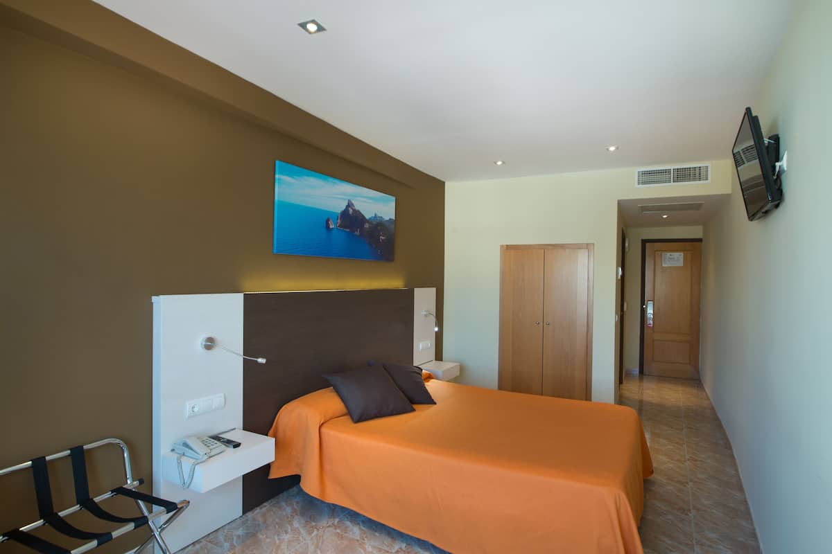 Habitación de hotel con cama, escritorio, silla, televisor montado en la pared y puerta que da a otra habitación.