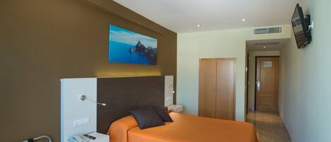 A hotel room with a bed, a desk, a chair, a TV mounted on the wall, and a door leading to another room.