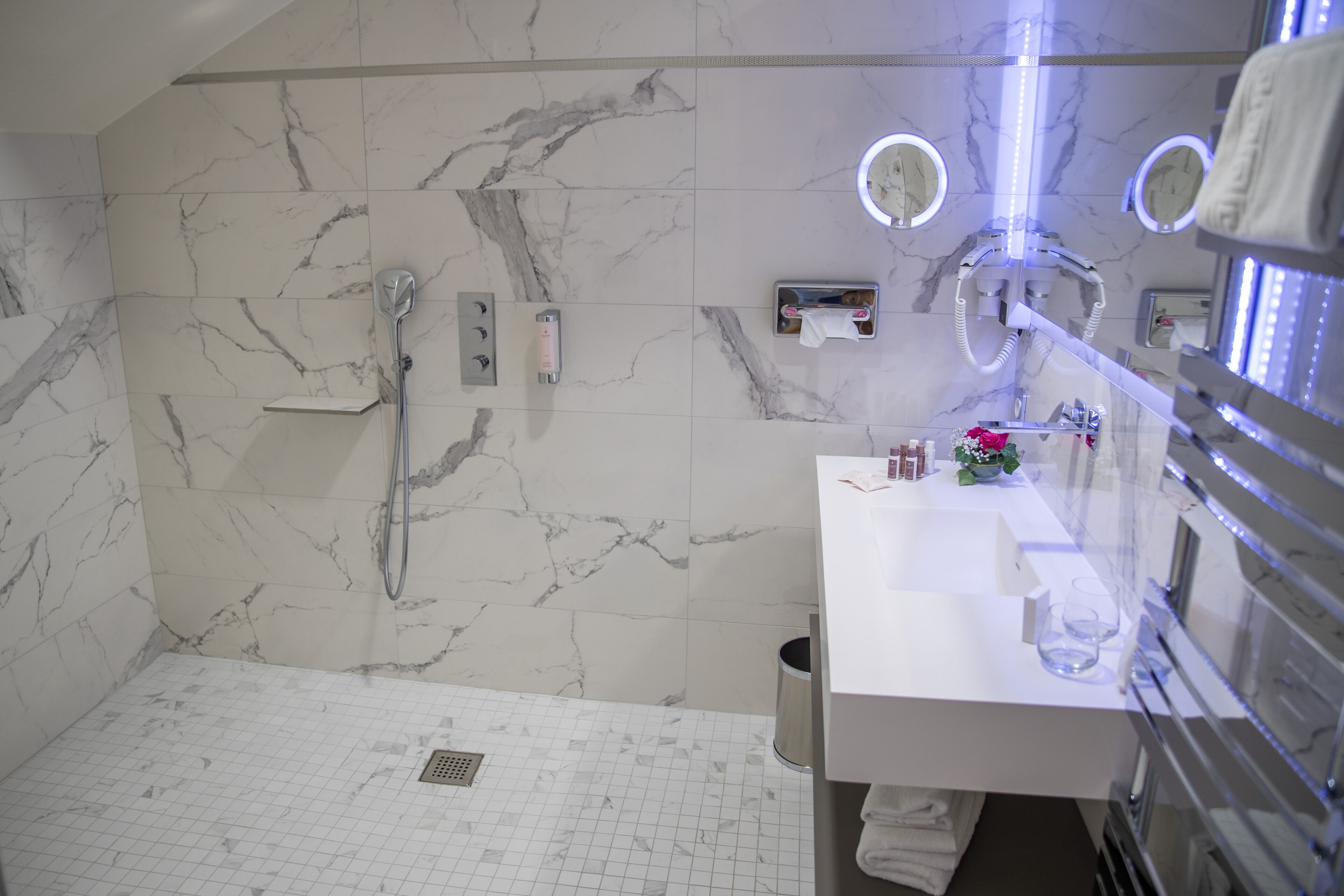 Une salle de bain moderne avec une douche en marbre blanc, un lavabo blanc avec un miroir et une paroi de douche en verre.