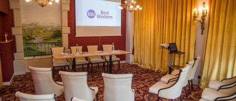 A conference room with a projector screen displaying "Best Western" branding, a long table with chairs, and a carpeted floor.