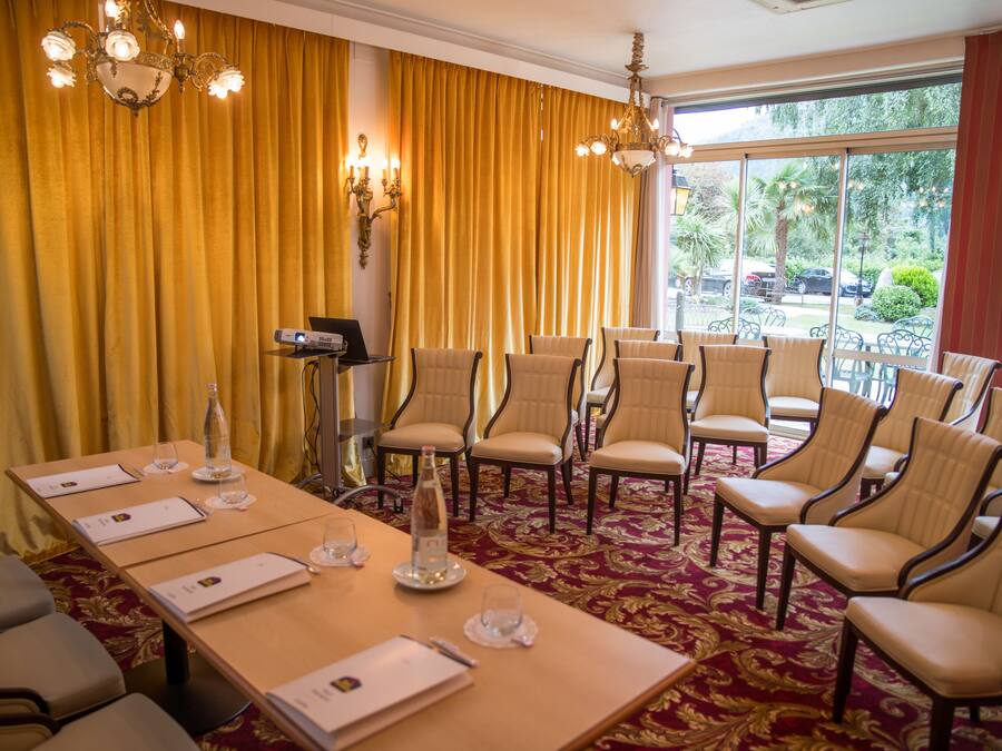 Una sala conferenze con un lungo tavolo, diverse sedie, un lampadario e vista sul verde attraverso ampie finestre.