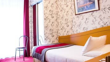 Ein Hotelzimmer mit Bett, Sessel, Fenster mit Vorhängen und einem Wandbild.