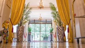 Una entrada imponente con candelabro, cortinas doradas y plantas en macetas.