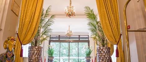 A grand entrance with a chandelier, golden curtains, and potted plants.