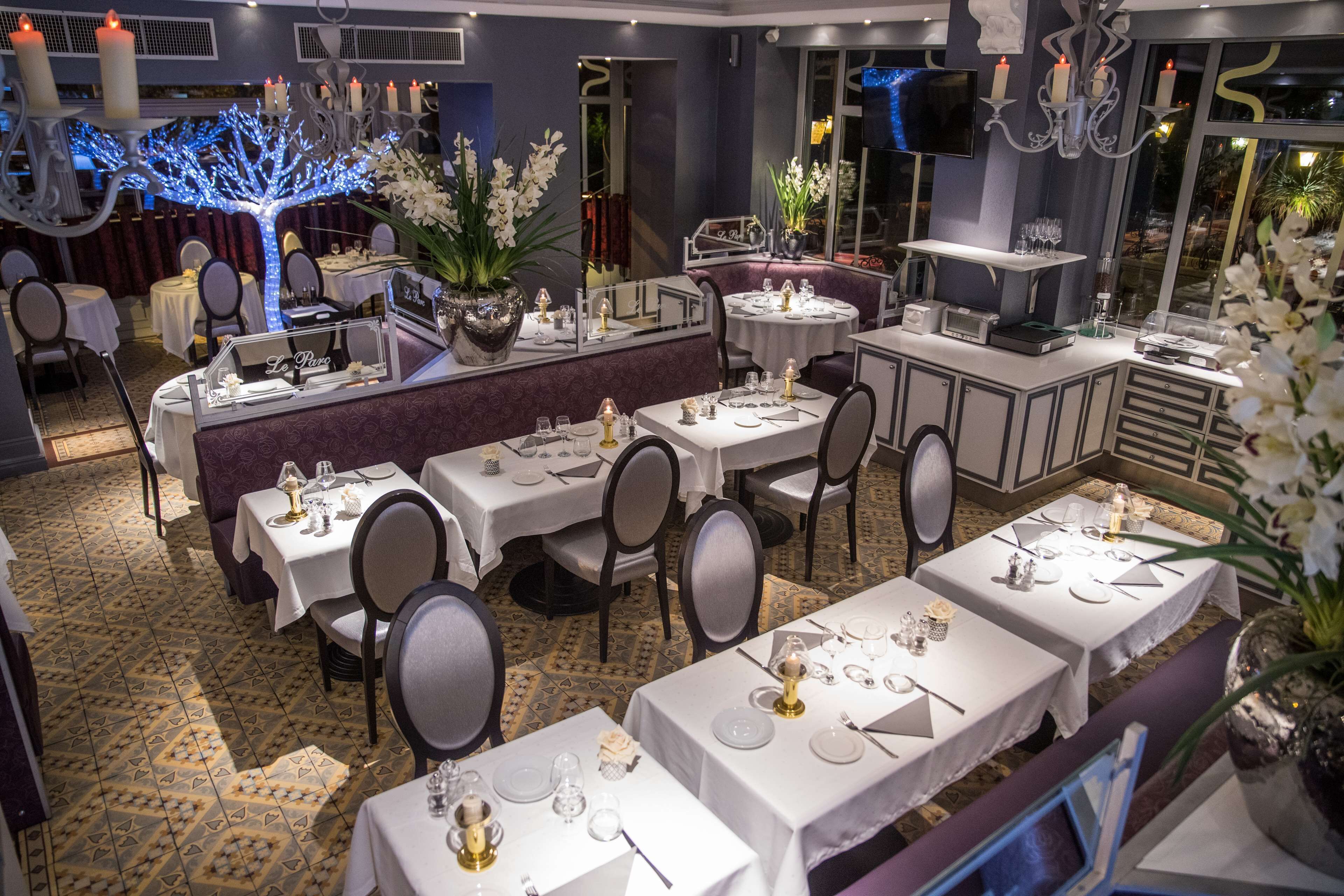 A restaurant with multiple tables set for dining, a bar area, and decorative elements like candles and plants.