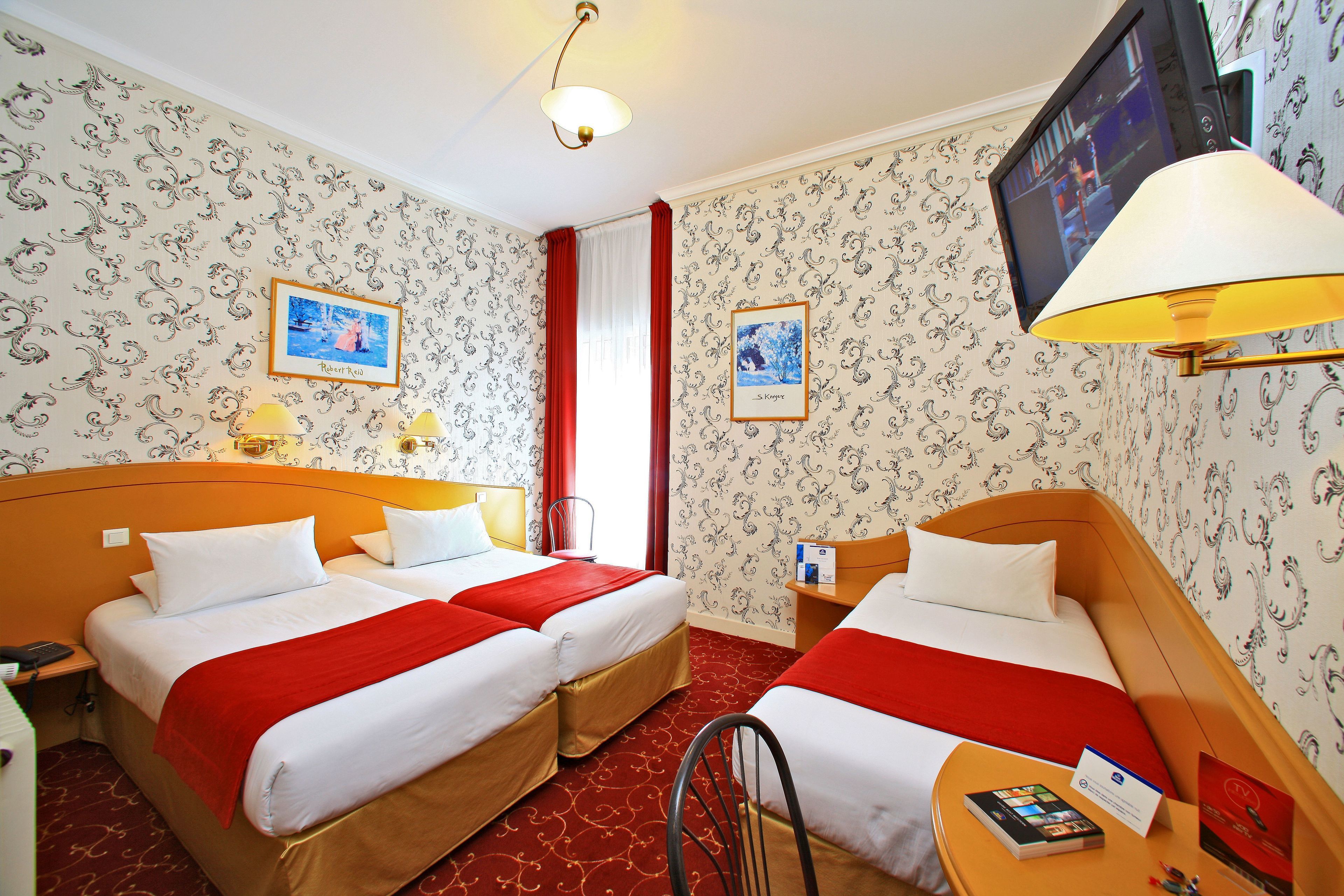 A hotel room with two beds, a TV, a desk with a lamp, and a chair.