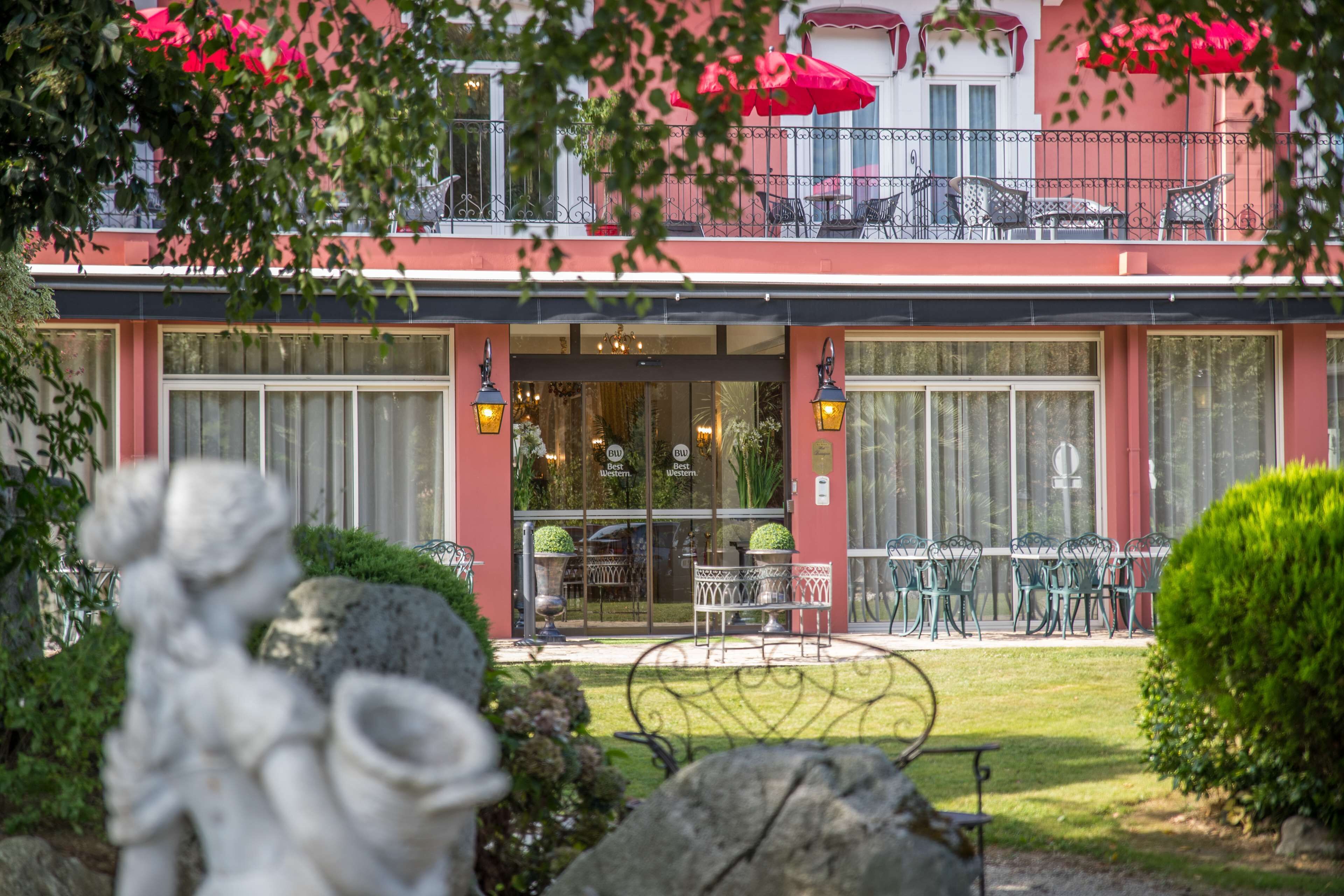 A hotel with a red facade, outdoor seating area with tables and chairs, and a balcony with red umbrellas.