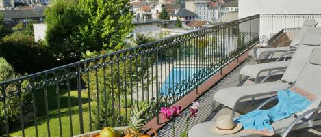 A balcony with a table set for breakfast, overlooking a pool and a scenic view of a town and mountains.