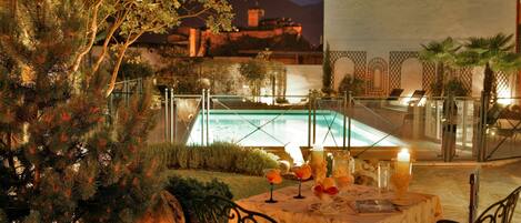 Un espace extérieur aménagé pour les repas, avec une table dressée pour deux personnes, donnant sur une piscine.