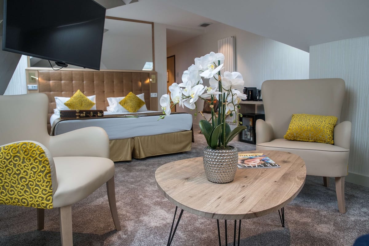 Une chambre d’hôtel moderne équipée d’un lit, de deux fauteuils, d’une table basse et d’un téléviseur.