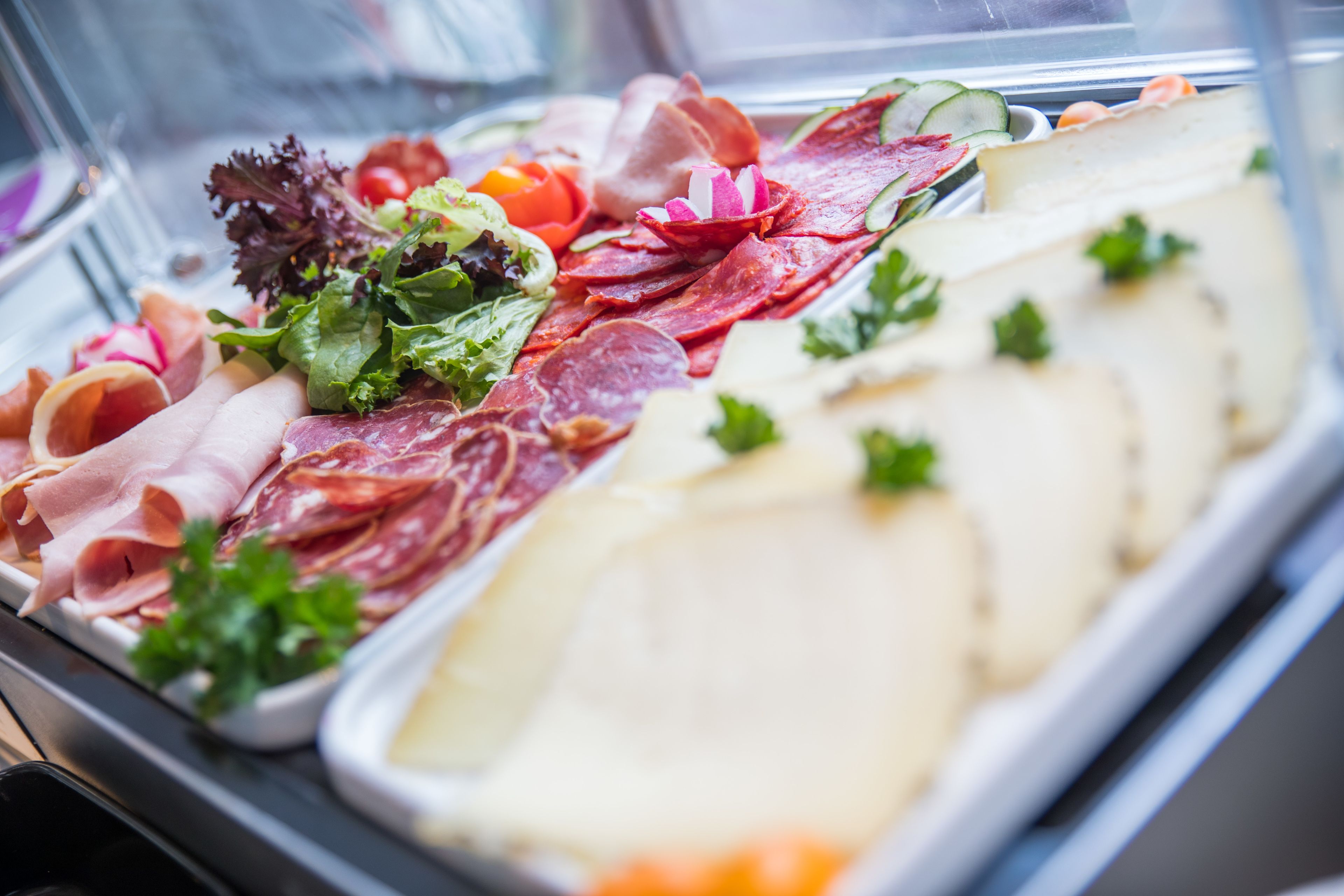 A variety of deli meats and cheeses displayed in a glass case.