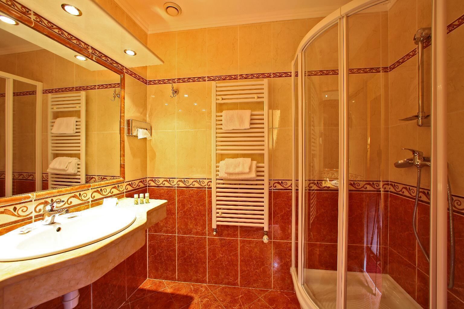 Un baño con lavamanos, espejo, toalleros y ducha.