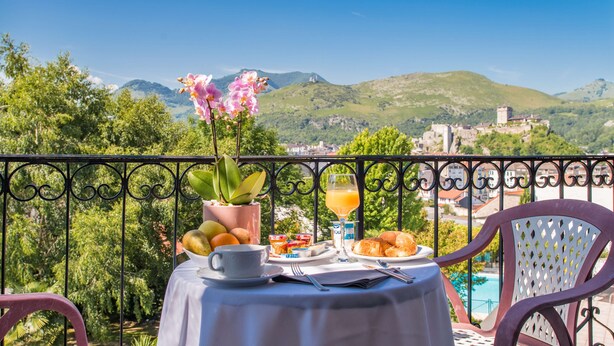 Una mesa preparada para el desayuno en un balcón con vistas a un paisaje pintoresco con montañas y un pueblo.