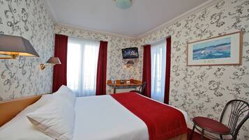A hotel room with a bed, a desk, a chair, a TV, and a painting on the wall.
