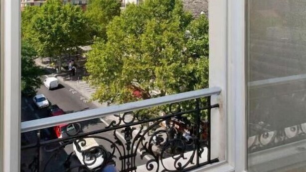Un balcone con vista su una strada residenziale, una ringhiera metallica e un cielo sereno.