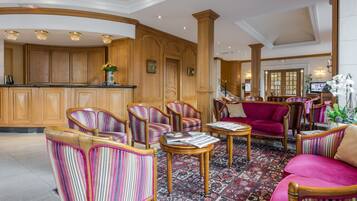 A lobby with wooden paneling, striped upholstered chairs, a red sofa, and a reception desk.