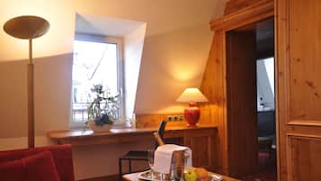 A cozy room with a wooden table, a red sofa, a lamp, a window with a view, and a door leading to another room.