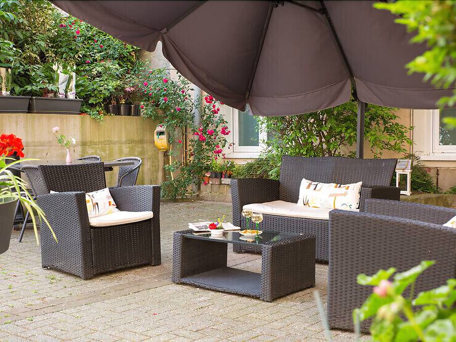 An outdoor seating area with wicker furniture and a table, surrounded by potted plants and flowers.