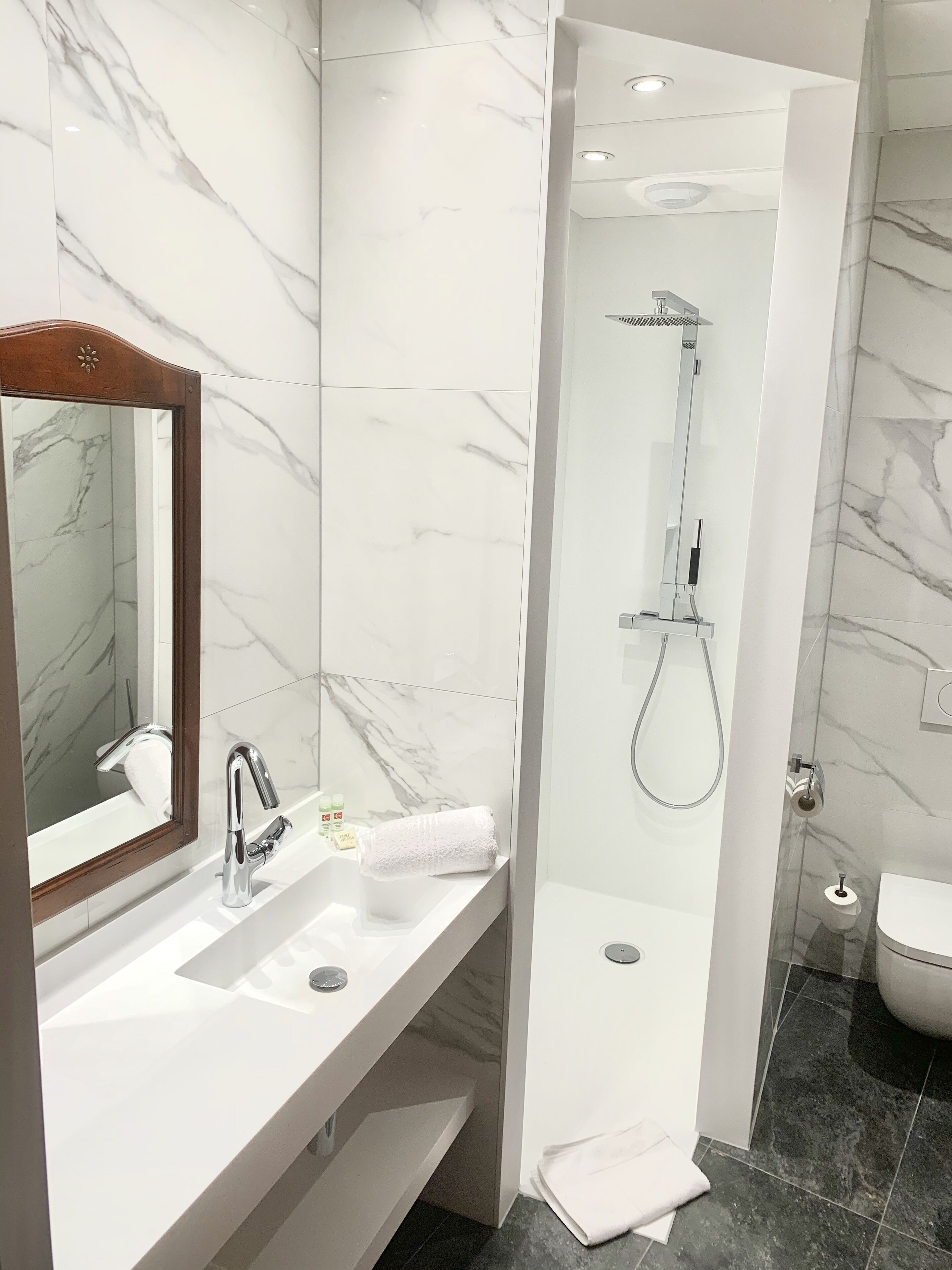 Une salle de bain moderne avec un meuble-lavabo en marbre, une douche équipée d’un pommeau de douche à main et des toilettes.