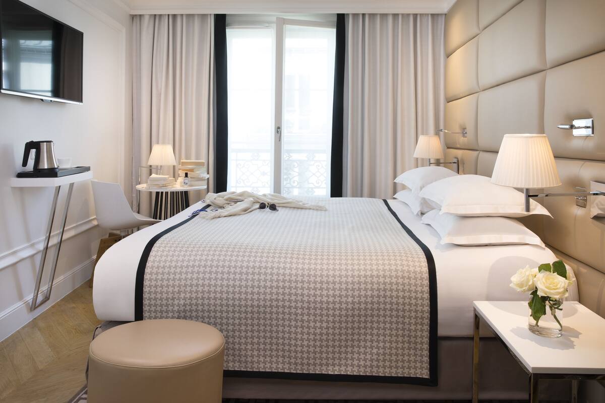 A hotel room with a large bed, two bedside tables, a TV, and a view of the outdoors.