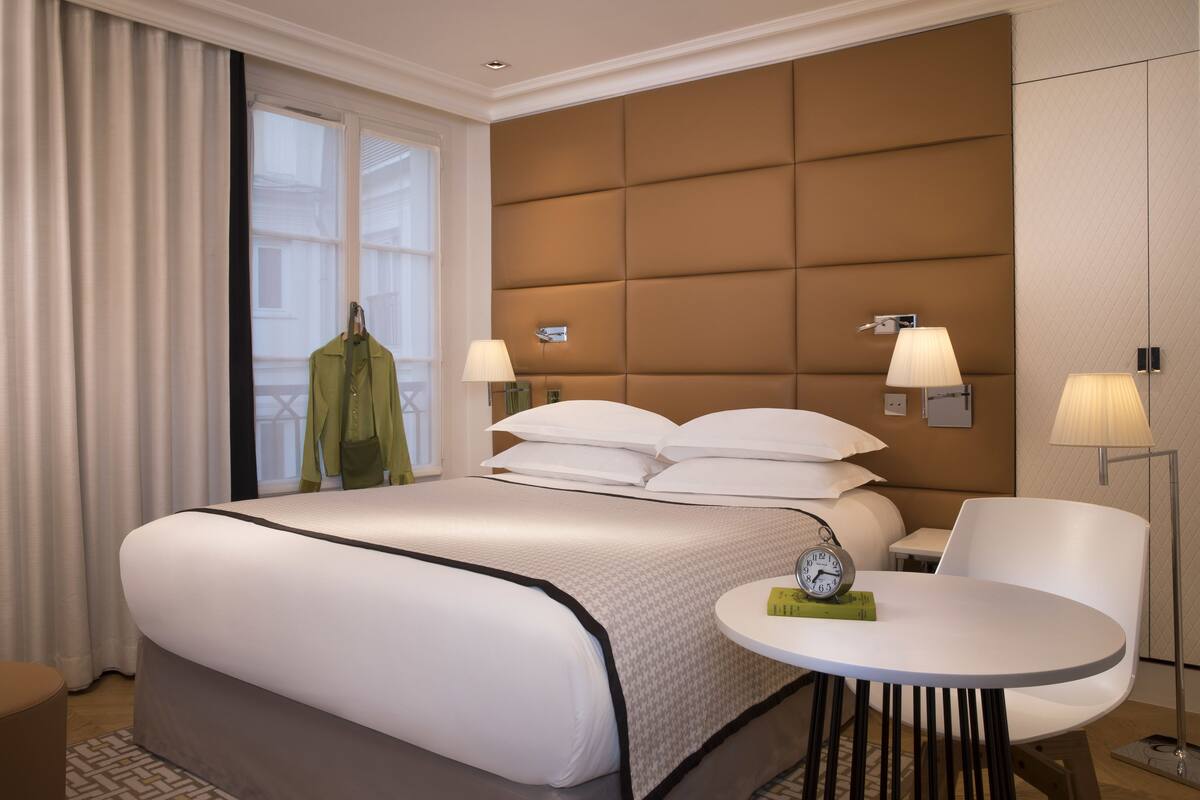A hotel room with a large bed, bedside lamps, a round table, and a view of the outside.