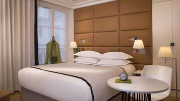 A hotel room with a large bed, bedside lamps, a round table, and a view of the outside.