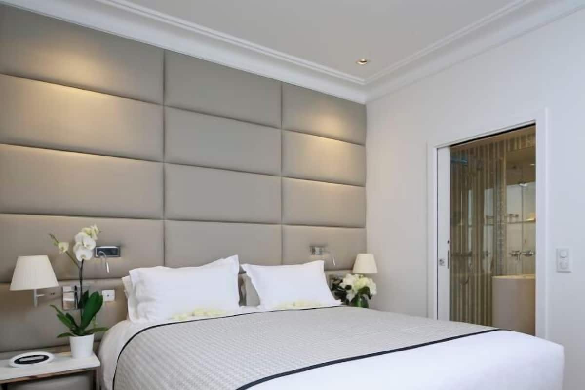 A hotel room with a large bed, bedside lamps, a nightstand, and a wall-mounted light fixture.