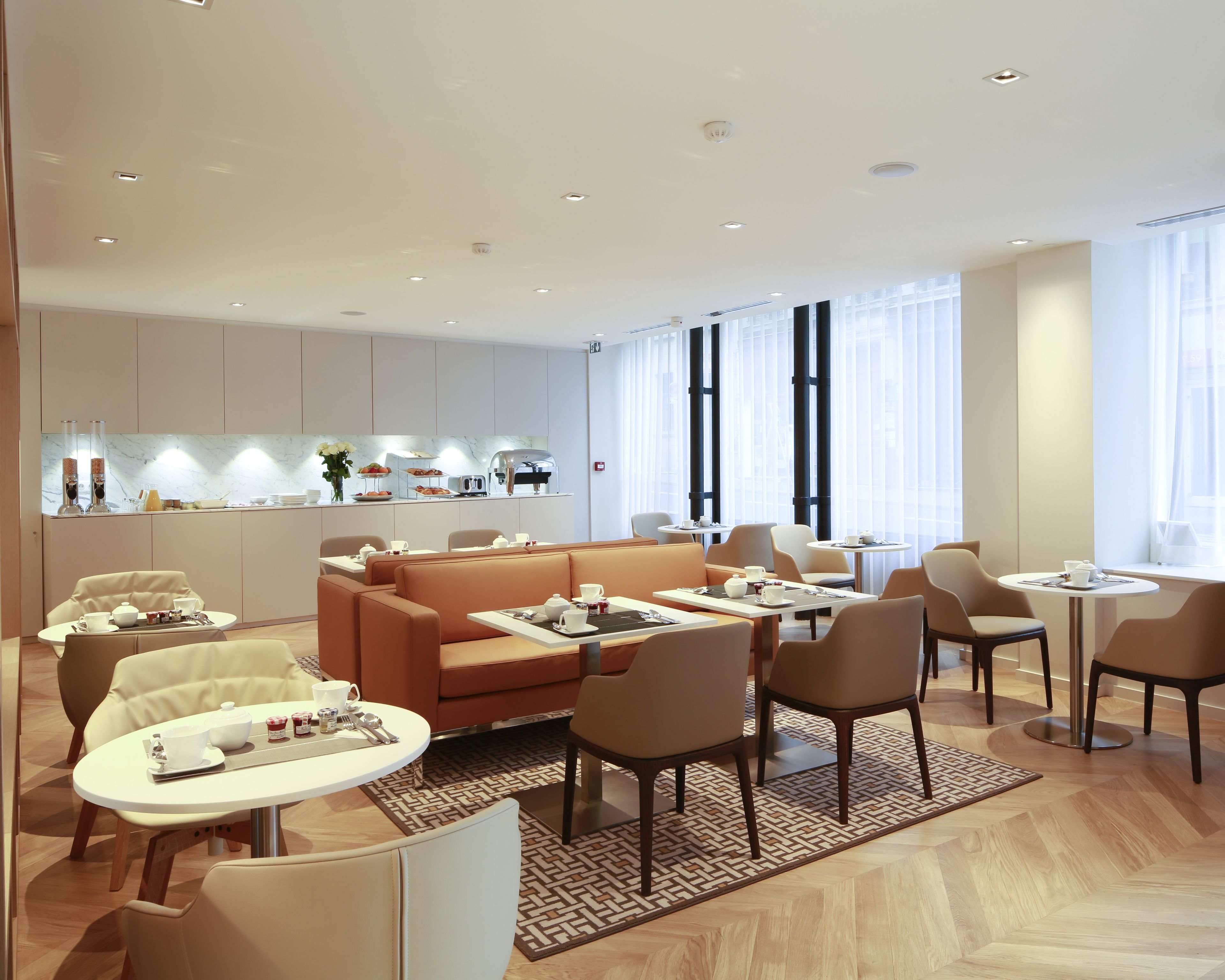 Un vestíbulo de hotel moderno con una zona de estar central, una kitchenette y amplias ventanas.