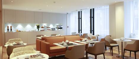 Un vestíbulo de hotel moderno con una zona de estar central, una kitchenette y amplias ventanas.