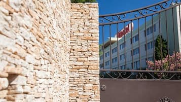 Un mur de pierre surmonté d’un portail en métal, qui reflète un bâtiment portant une enseigne indiquant « Hôtel ».