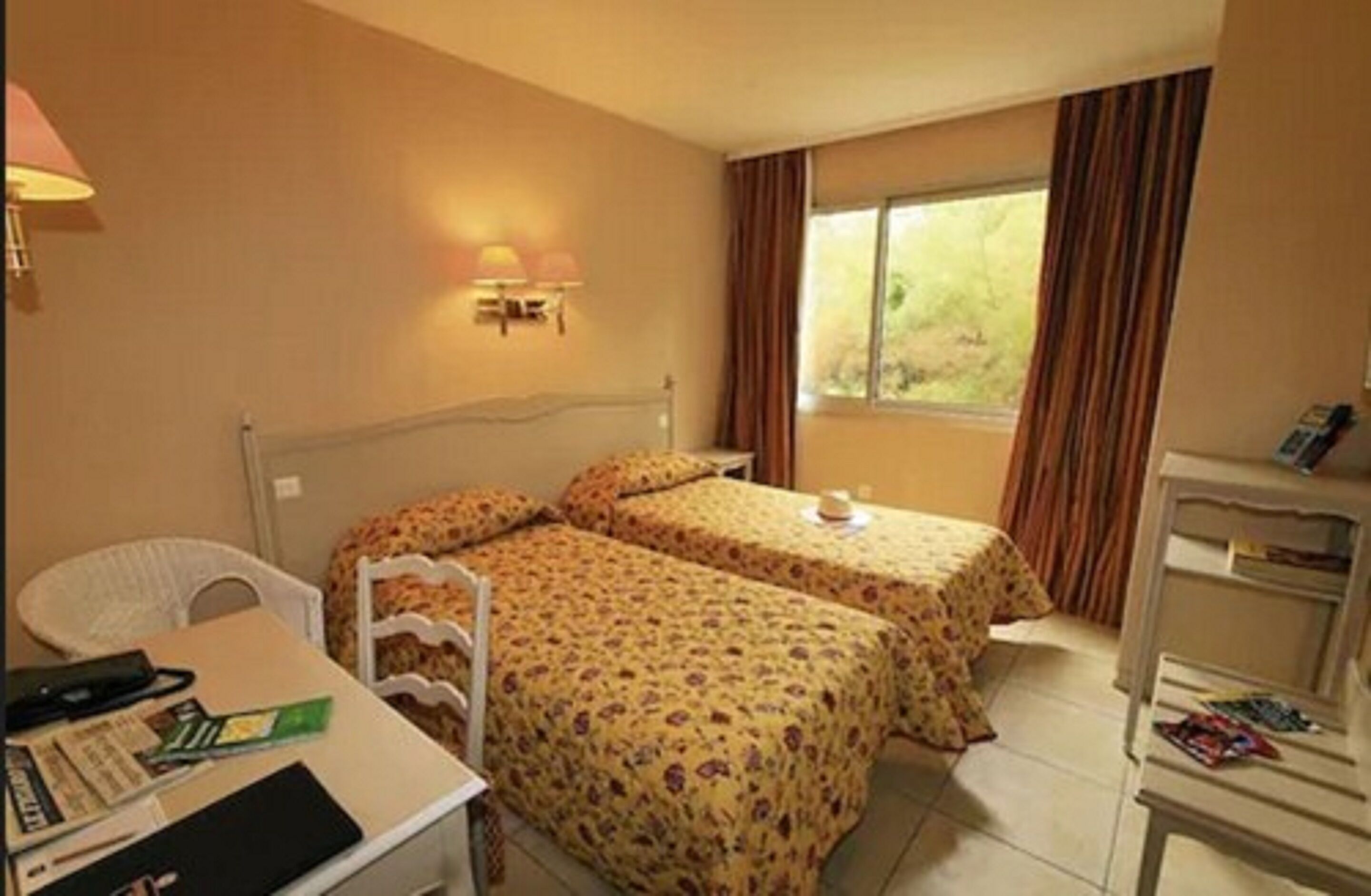 Habitación de hotel con dos camas, un escritorio, una silla y una ventana con cortinas.