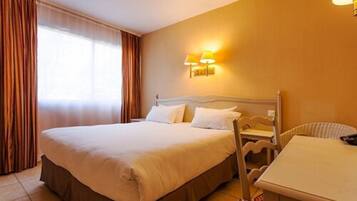 A hotel room with a bed, a chair, a table, and a lamp.