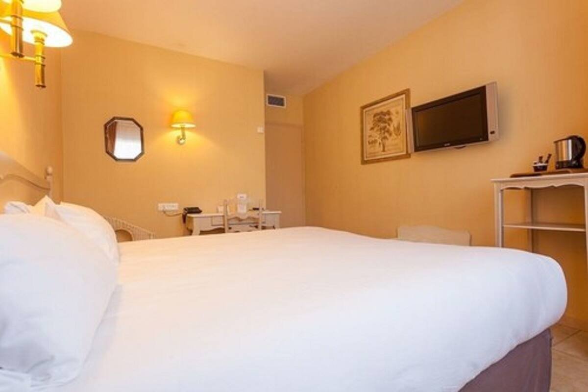 Una habitación de hotel con una cama grande, un escritorio, una silla, un televisor y una lámpara fijada a la pared.
