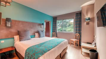 Ein Schlafzimmer mit Bett, Nachttischen, einem Sessel, einem Schreibtisch, einem Fenster und Blick auf Grünflächen.