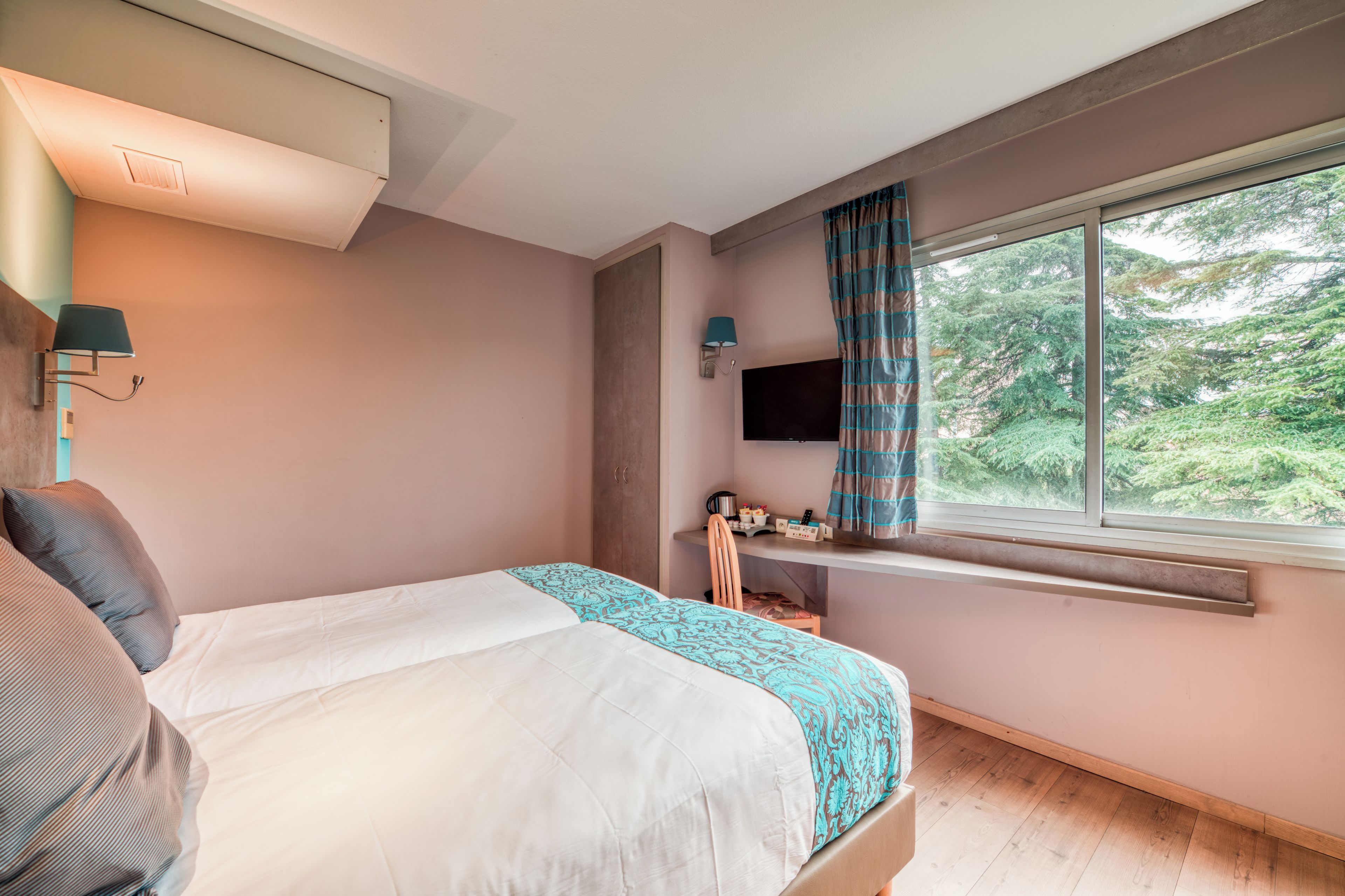 A bedroom with a bed, a desk with a computer, a TV, and a window with curtains.