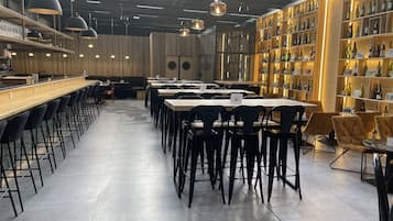 A modern restaurant interior with long communal tables, black chairs, and a wine display on the right.