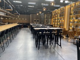 Un interior de restaurante moderno con mesas comunitarias largas, sillas negras y una exhibición de vinos a la derecha.