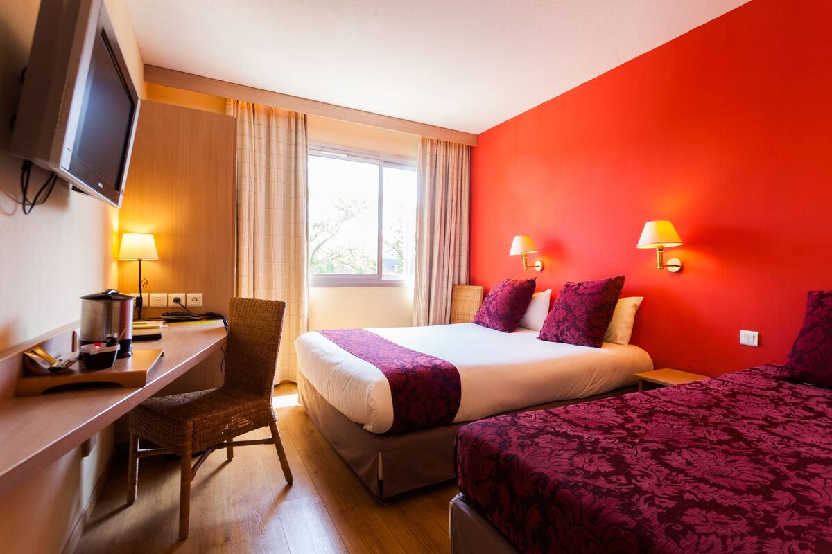 Una habitación de hotel con cama, escritorio, silla, televisor y dos lámparas de noche.