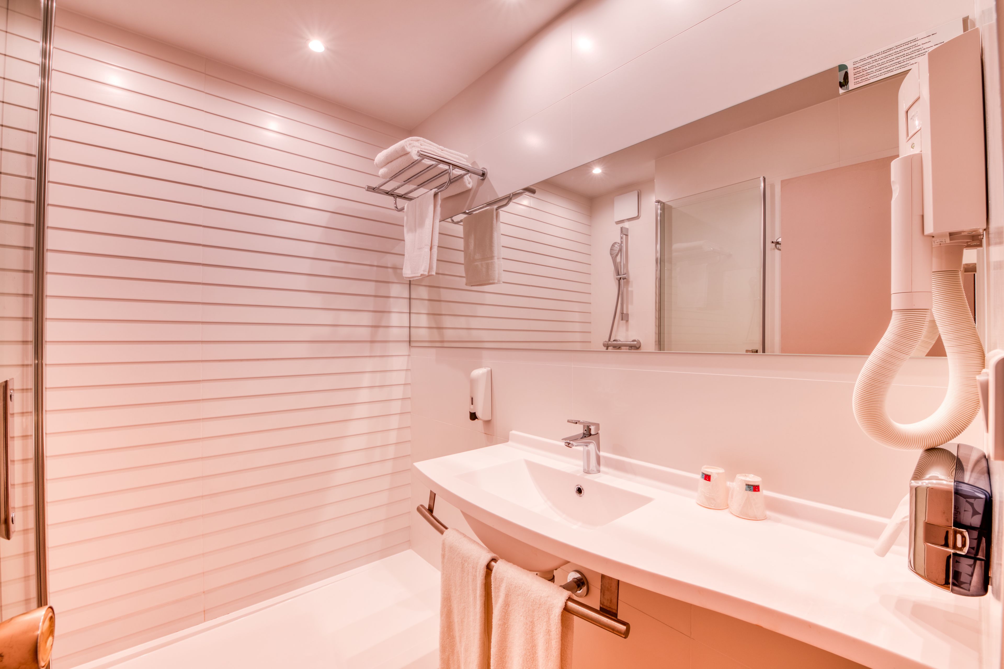 A modern bathroom with a large mirror, a shower area, and a vanity with a sink.